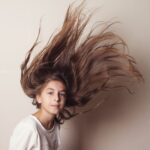 Portrait of a girl with long hair in motion against a plain background.