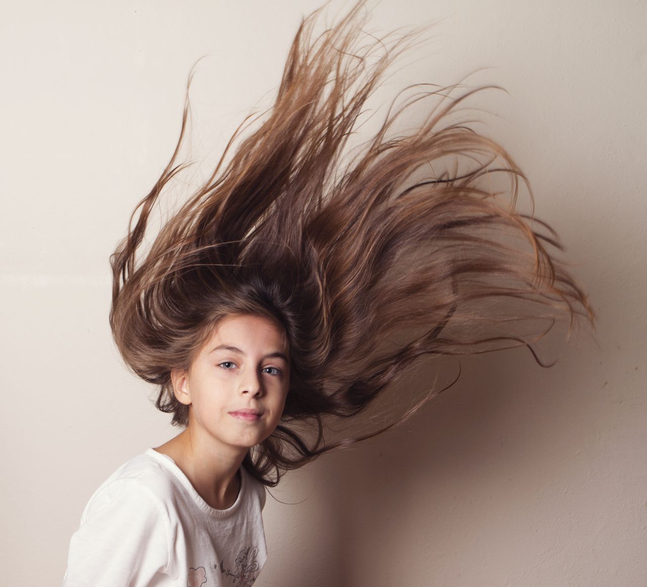 Portrait of a girl with long hair in motion against a plain background.